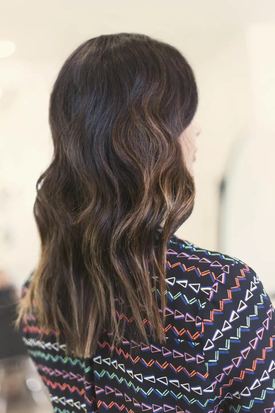 Cabelo castanho com ondas suaves e iluminação nas pontas, visto de costas