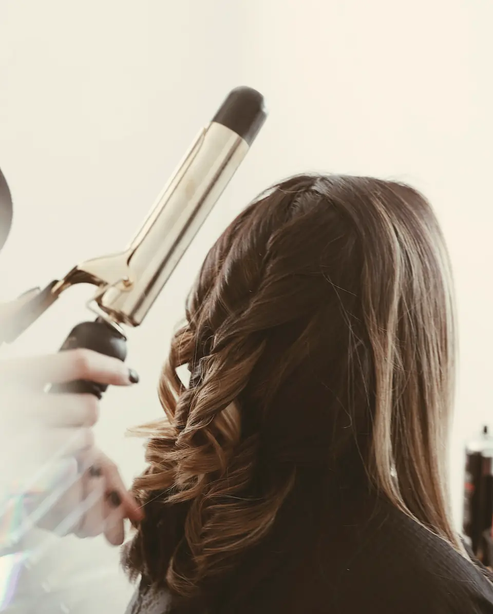 Profissional modelando ondas com babyliss em um cabelo castanho longo