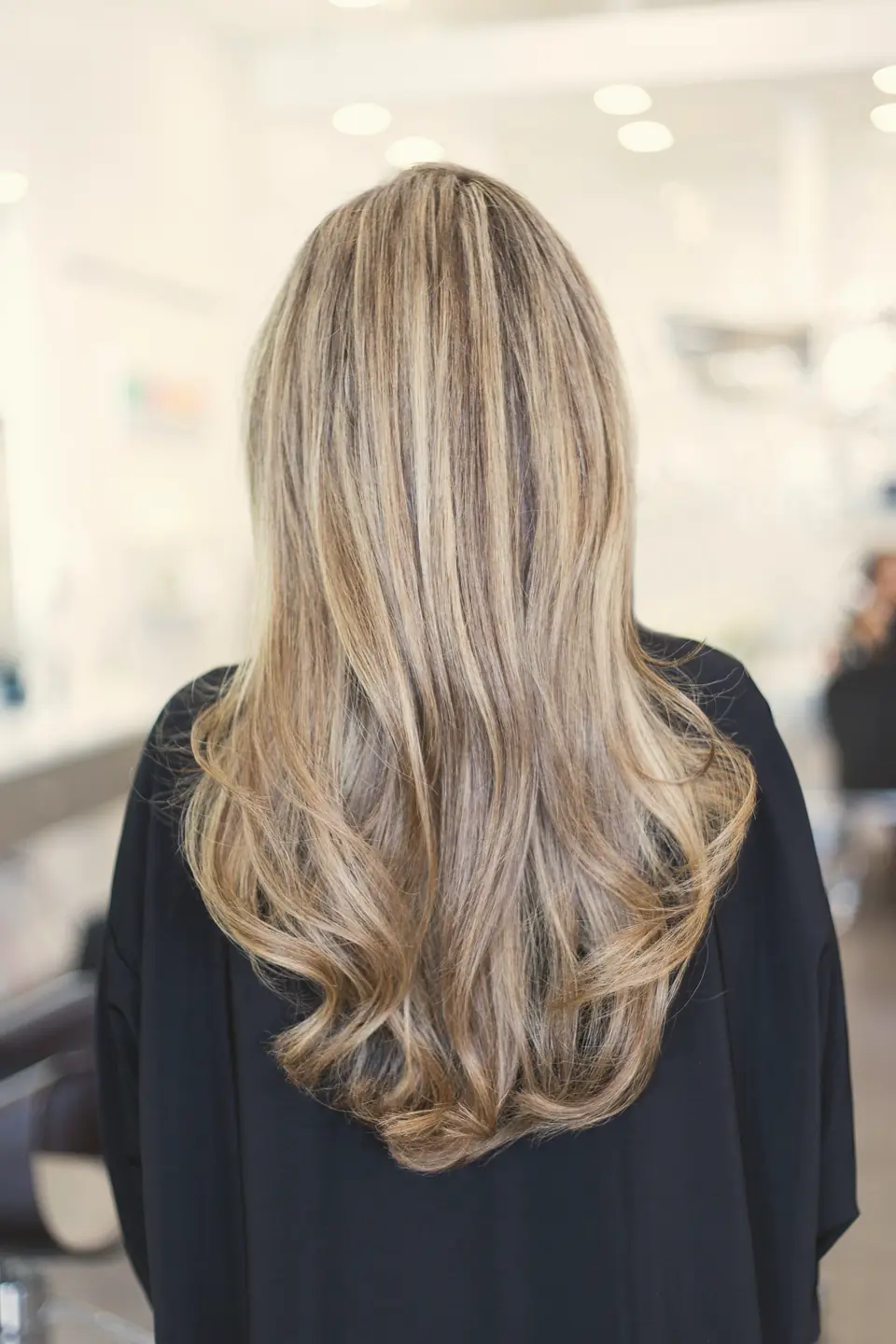 Cabelo longo com mechas loiras e morenas iluminadas, visto de costas no salão
